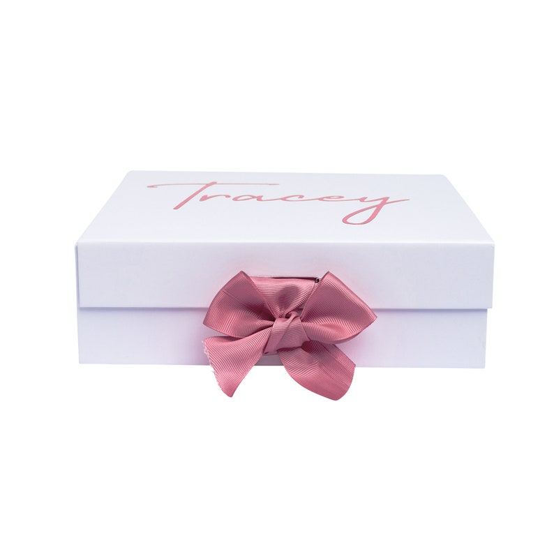 May include: White gift box with a pink ribbon and the name "Tracey" printed on the top.