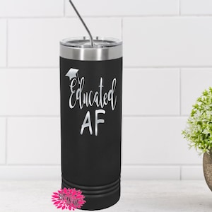 May include: A black insulated tumbler with a silver lid and straw. The tumbler features the words "Educated AF" in a script font with a graduation cap graphic. The tumbler is cylindrical and sits on a white surface.