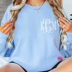 May include: A light blue sweatshirt with a white monogram of the letters "KCM" on the front.