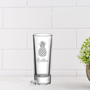 May include: A clear glass shot glass with a pineapple design and the name "Heather" etched on the front.