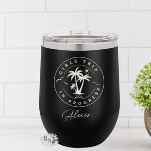 May include: Black stainless steel wine tumbler with a white graphic of palm trees and the text "Girls Trip In Progress 2024" with the name "Alexis" below the graphic.