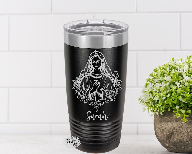 Puede incluir: Un vaso de acero inoxidable negro con un dise&ntilde;o blanco de la Virgen Mar&iacute;a con rosas y el nombre "Sarah" en la parte inferior.