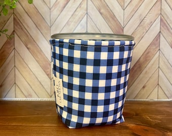 May include: A glass jar wrapped in a blue and white gingham fabric. The fabric has a tag that reads "Jojo Creations". The jar sits on a wooden surface with a chevron pattern background. The jar is designed to hold items.