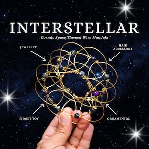 May include: Gold wire mandala with black, purple and grey beads. The mandala is a cosmic space themed design. The text "INTERSTELLAR Cosmic Space Themed Wire Mandala" is at the top of the image. The text "JEWELERY, FIDGET TOY, ORNAMENTAL, HAIR ACCESSORY" is around the mandala.