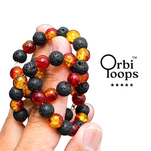 May include: A bracelet featuring alternating black porous lava stone beads and translucent amber-colored glass beads. The text Orbi Loops is printed in black to the right of the jewelry, accompanied by a row of five black stars below the text.