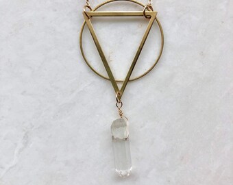 May include: Gold geometric necklace with a clear quartz crystal pendant. The necklace features a circle and triangle design.