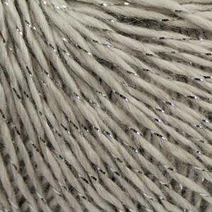 May include: Close-up of a skein of light gray yarn with silver metallic threads. The yarn is tightly twisted, creating a textured surface. The metallic threads add a subtle sparkle to the yarn, suitable for knitting or crochet projects.