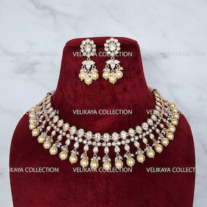 Peut inclure: Un collier en or avec un design multi-couches composé de pierres claires et de perles. Le collier est présenté sur un fond de velours rouge avec des boucles d'oreilles assorties.