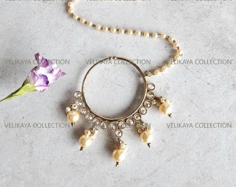 May include: A gold nose ring with a circular design and a chain of pearls. The nose ring has a cluster of pearls hanging from the bottom.