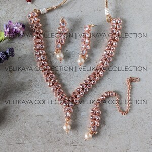 May include: A rose gold necklace set with a delicate chain, pink crystal teardrop embellishments, and pearl accents. The set includes a necklace, earrings, and a bracelet.