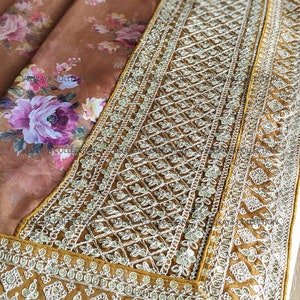 Op de afbeelding: Een bruine zijden sari met een bloemenprint en een gouden geborduurde rand. De rand heeft een geometrisch patroon met pailletten en kralen.