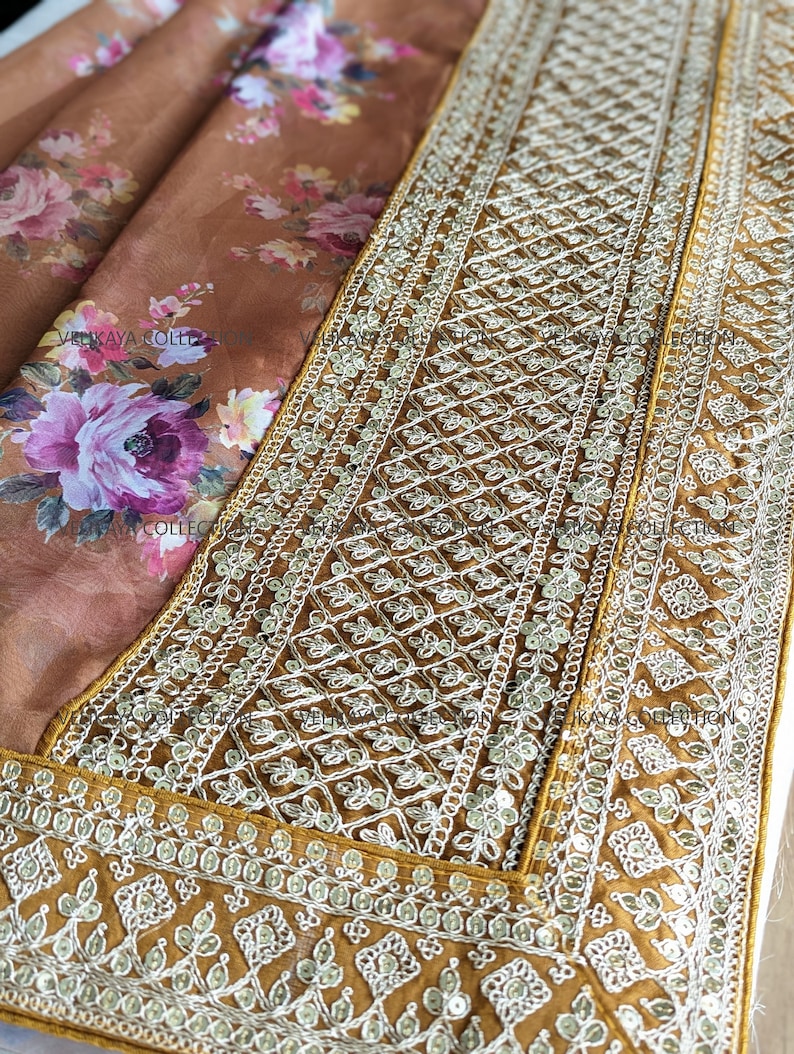 Op de afbeelding: Een bruine zijden sari met een bloemenprint en een gouden geborduurde rand. De rand heeft een geometrisch patroon met pailletten en kralen.