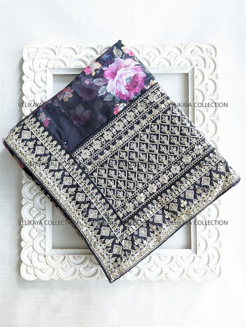 Op de afbeelding: Zwarte zijden sari met bloemenprint en zilveren borduurwerk. De sari heeft een geometrisch patroon en is ingelijst in een wit houten frame.