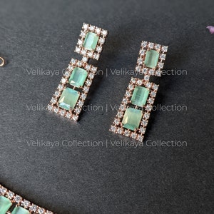 May include: A rose gold necklace and earrings set with green and clear stones. The necklace has a row of rectangular green stones with clear stones around them. The earrings have three rectangular green stones with clear stones around them.