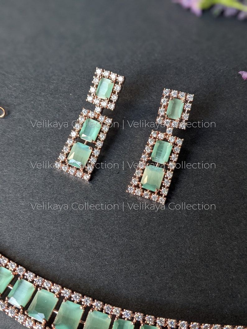May include: A rose gold necklace and earrings set with green and clear stones. The necklace has a row of rectangular green stones with clear stones around them. The earrings have three rectangular green stones with clear stones around them.