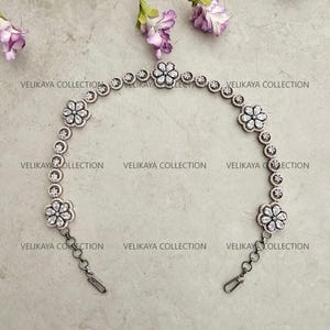 May include: A silver chain necklace with a floral design. The necklace has a clasp closure and is adorned with clear cubic zirconia stones.