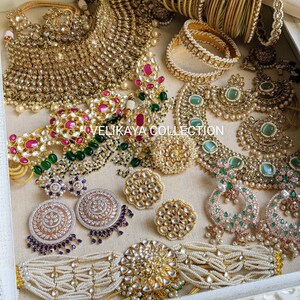 May include: A set of Indian bridal jewelry featuring a gold and pearl necklace, earrings, bangles, and a choker. The jewelry is decorated with green and pink stones.