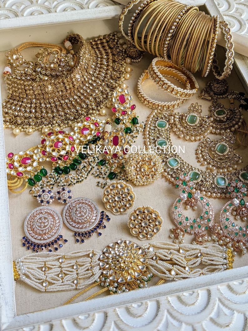 May include: A set of Indian bridal jewelry featuring a gold and pearl necklace, earrings, bangles, and a choker. The jewelry is decorated with green and pink stones.