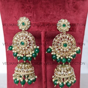 Puede incluir: Un conjunto de joyas de novia indias de oro y verde con un collar, pendientes y un maang tikka. El collar tiene un colgante redondo con dise&ntilde;os intrincados y cuentas verdes. Los pendientes tienen un dise&ntilde;o similar con un colgante redondo y cuentas verdes. El maang tikka tiene un peque&ntilde;o colgante con cuentas verdes.