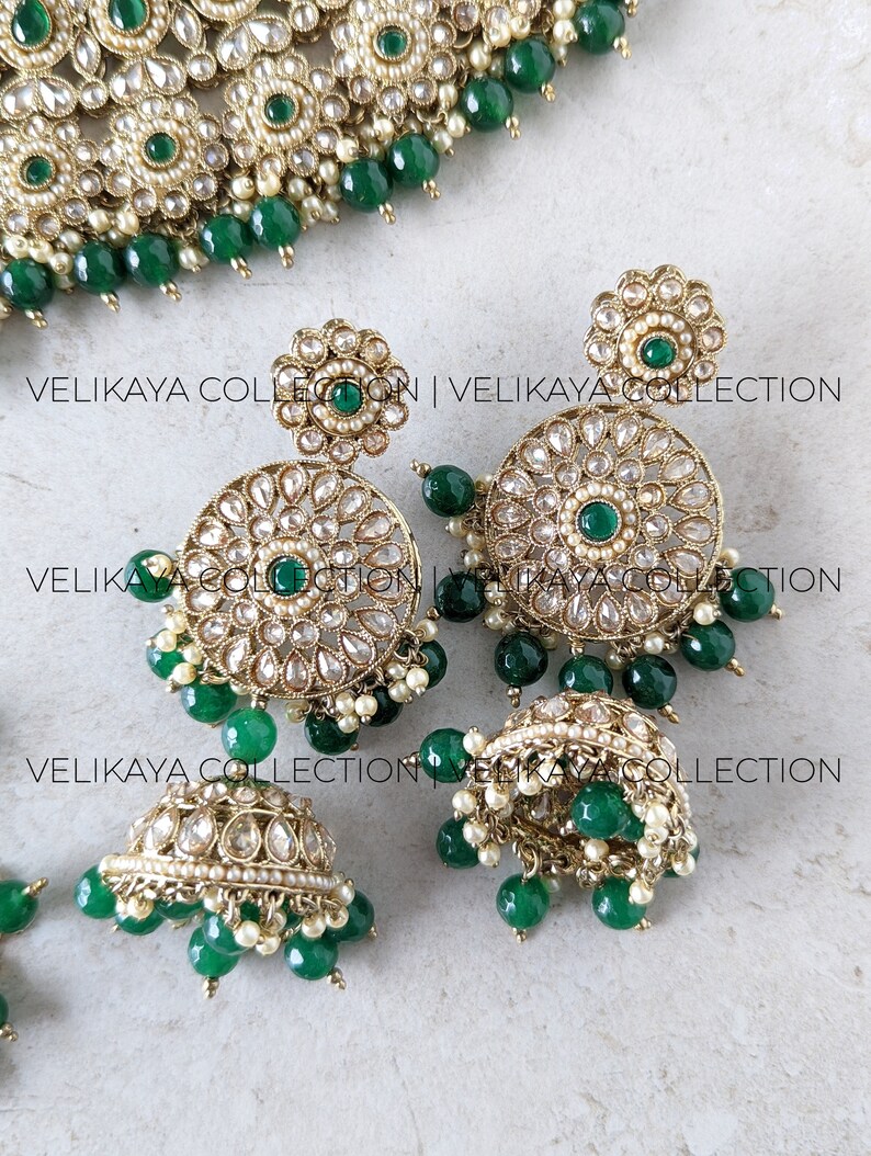 Puede incluir: Un conjunto de joyas de novia indias de oro y verde con un collar, pendientes y un maang tikka. El collar est&aacute; adornado con perlas y piedras verdes, y los pendientes son redondos con un dise&ntilde;o floral.