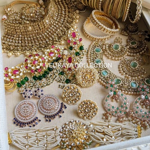 May include: A set of Indian bridal jewelry featuring a gold and pearl necklace, earrings, bangles, and a choker. The jewelry is decorated with green and pink stones.