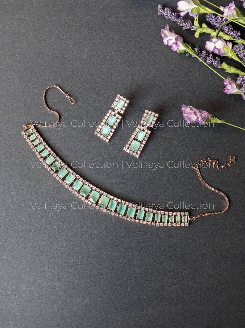 May include: A delicate gold necklace with a row of light green rectangular stones and clear rhinestones. Matching earrings with light green stones and rhinestones.