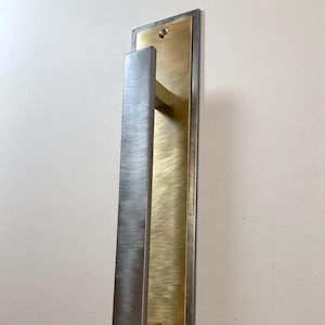 May include: A white ceramic mug with a black handle and the text "But First, Coffee" in a bold, black font. The mug is set against a blurred background, suggesting a cozy setting.