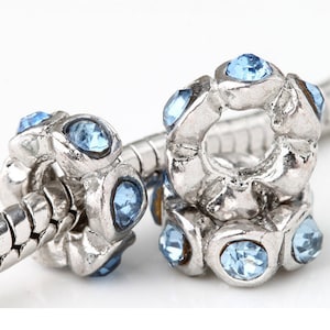 May include: Two silver charm beads with light blue crystal accents. The beads are designed to fit on a charm bracelet.