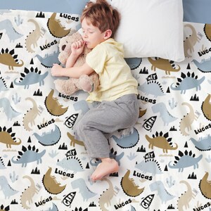 May include: A white baby blanket with a repeating pattern of blue and brown dinosaurs. The name "Lucas" is printed on the blanket in black letters.