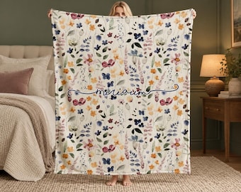 Puede incluir: Una manta rectangular con fondo color crema y un estampado floral estilo acuarela en tonos rosa, amarillo, azul y verde. La palabra "miriam" está impresa en una tipografía cursiva de color azul oscuro en el centro.