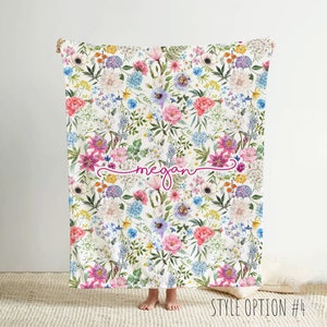 May include: A white blanket with a floral pattern in shades of pink, blue, and yellow. The blanket has the name "Megan" written in pink cursive script.