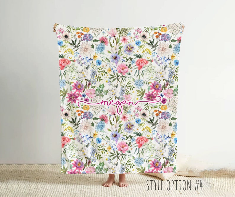 May include: A white blanket with a floral pattern in shades of pink, blue, and yellow. The blanket has the name "Megan" written in pink cursive script.