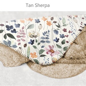 May include: Tan sherpa throw blanket with a floral print featuring watercolor flowers in shades of pink, blue, and orange on a white background. The blanket is folded in half, showing both the sherpa and floral sides.
