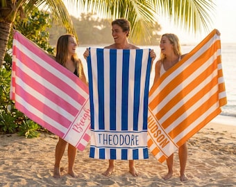 May include: Three rectangular beach towels featuring vertical stripes in pink, blue, and orange, each with a white border. The pink towel is personalized with the name Breigh, the blue with Theodore, and the orange with HUDSON.
