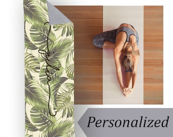 May include: Personalized yoga mat with a tropical leaf pattern in shades of green and white. The mat has the name "Julia" written on it in black cursive.