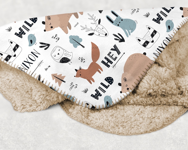 May include: White fleece blanket with a woodland animal print. The blanket features a fox, deer, owl, bear, rabbit, raccoon, and birds. The text "Wild Hey Nixon" is printed on the blanket.