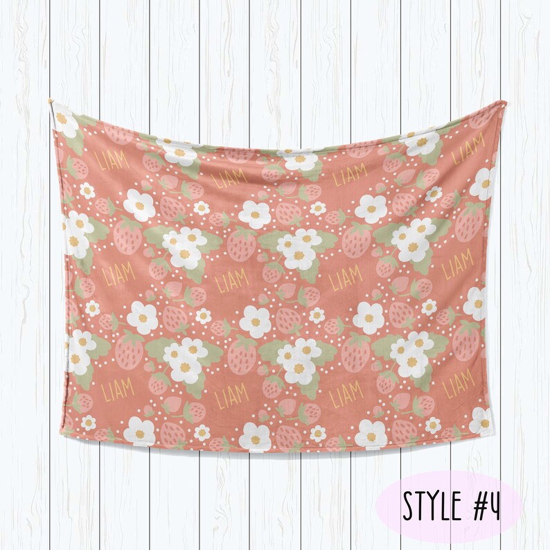 Puede incluir: Una manta de beb&eacute; rosa y blanca con un patr&oacute;n de fresas y flores. El nombre "Liam" se repite en toda la manta. STYLE #4