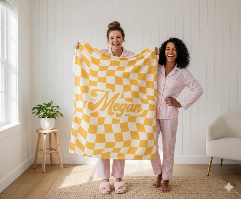 Puede incluir: Una manta a cuadros amarillos y blancos con el nombre "Megan" en una fuente retro. Dos personas con pijamas de rayas rosas sostienen la manta. La manta es un elemento de decoraci&oacute;n del hogar.