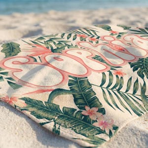 May include: A rectangular beach towel featuring a cream-colored background with a tropical pattern of green palm leaves and pink hibiscus flowers. The name Sophia is printed across the center in large, stylized, bubble-style pink lettering.