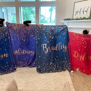 May include: Three personalized blankets with a blue and purple ombre background and gold glitter. The blankets have the names "Whitney", "Bradley", and "Dylan" written in gold script.