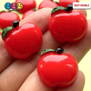 May include: Three red apple shaped resin cabochons with green leaves and black stems. NOT EDIBLE.