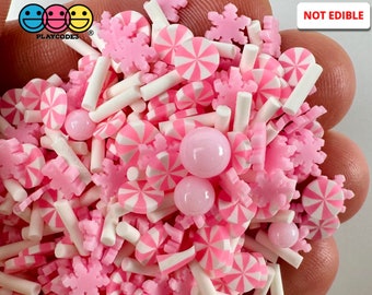 May include: Pink and white candy cane sprinkles, snowflake sprinkles, and white sticks. The sprinkles are in a hand and the text "NOT EDIBLE" is in the top right corner of the image.