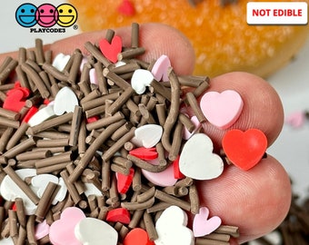 May include: A close-up of brown sprinkles and pink, white, and red heart sprinkles. The text "NOT EDIBLE" is visible in the upper right corner of the image.