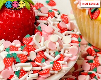 May include: A close-up of a variety of colorful sprinkles and decorations, including strawberry shapes, white sticks, and pink and white circles. A large, red strawberry is in the background. The text "NOT EDIBLE" is visible.