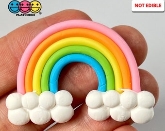 May include: A rainbow-colored clay rainbow with white clouds on either side. The rainbow is made of pink, orange, yellow, green, blue, and purple clay. The clouds are made of white clay. The rainbow is not edible. "NOT EDIBLE" is written in red letters on a white background in the upper right corner of the image.