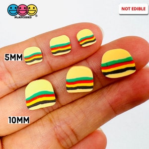 May include: Five miniature hamburger-shaped polymer clay charms in various sizes, ranging from 5mm to 10mm. The charms are yellow with green, red, and black stripes. The text "NOT EDIBLE" is visible in the upper right corner of the image.