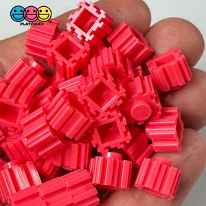 May include: A pile of bright pink plastic building blocks with a variety of shapes and sizes. The blocks are designed to connect together to create structures.