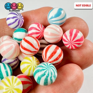 May include: A collection of colorful swirl patterned gumball machine balls. The balls are made of plastic and are not edible.  The balls are in a variety of colors, including pink, red, blue, green, yellow, and purple.