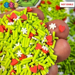 May include: Green, red, and white sprinkles in the shape of hearts, snowflakes, and long, thin sticks. The sprinkles are in a hand, and the text "NOT EDIBLE" is in the upper right corner of the image.