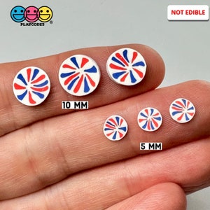 May include: A set of five red, white, and blue swirl patterned, round, flat, plastic candy-like decorations. The decorations are in two sizes, 10 mm and 5 mm. The text "NOT EDIBLE" is in the upper right corner of the image.
